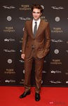 Robert Pattison vistiendo un traje marrón con corbata gris