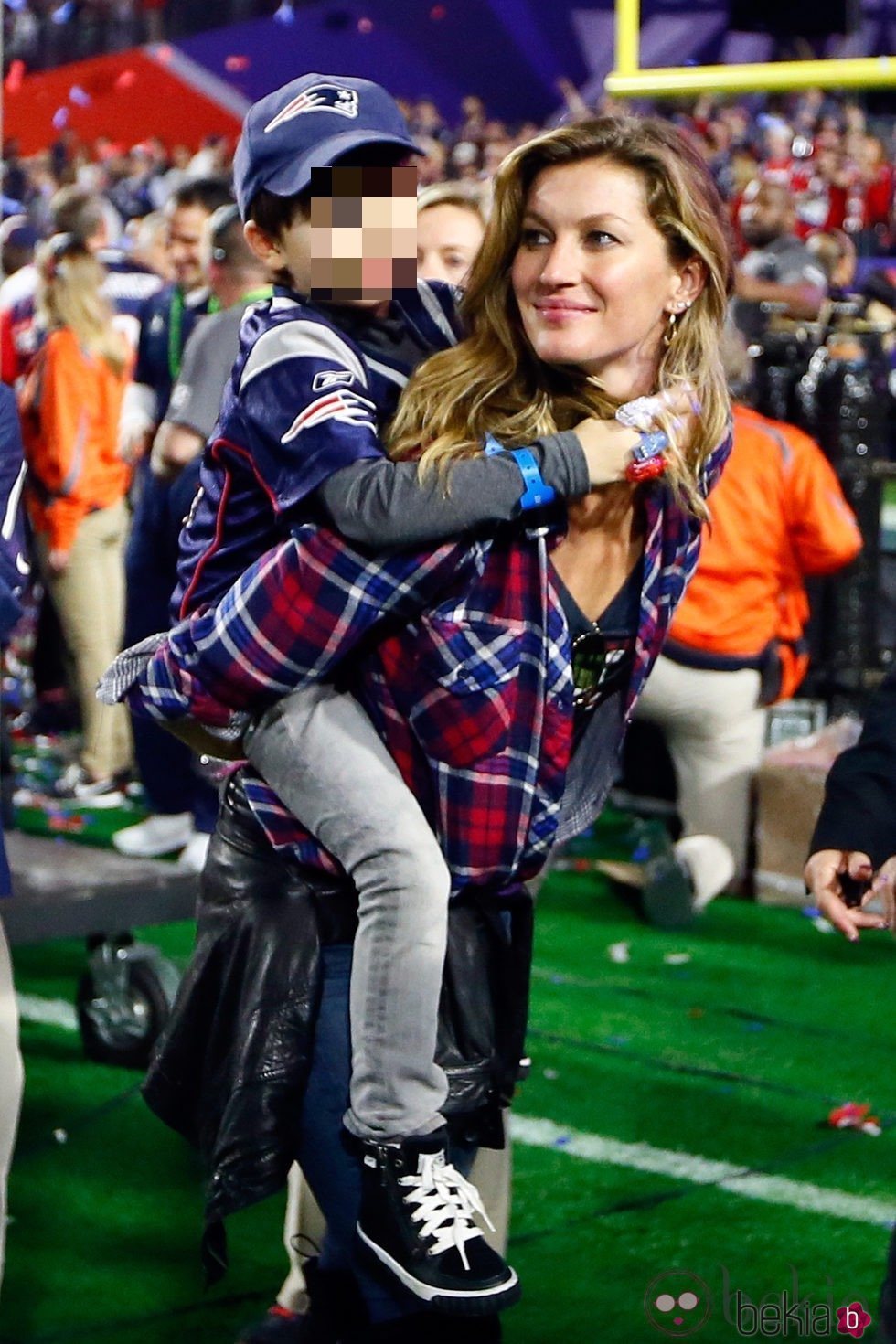 Gisele Bundchen con camisa de cuadros y vaqueros en un partido de la Super Bowl con su hijo