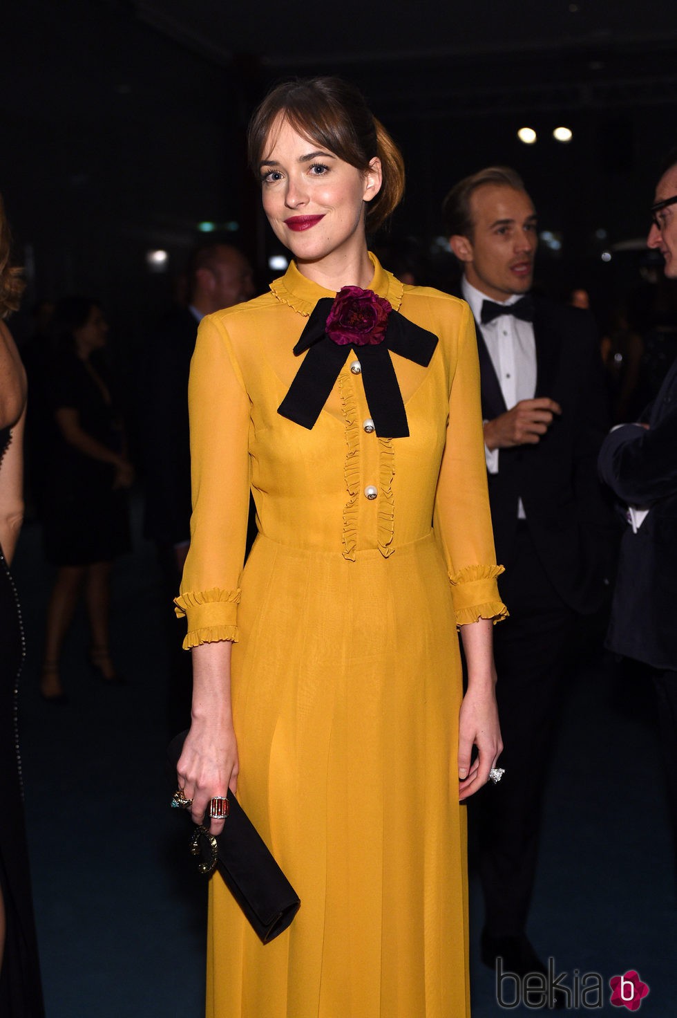 Dakota Johnson con vestido mostaza con lazada burdeos al cuello de la colección Crucero 2016 
