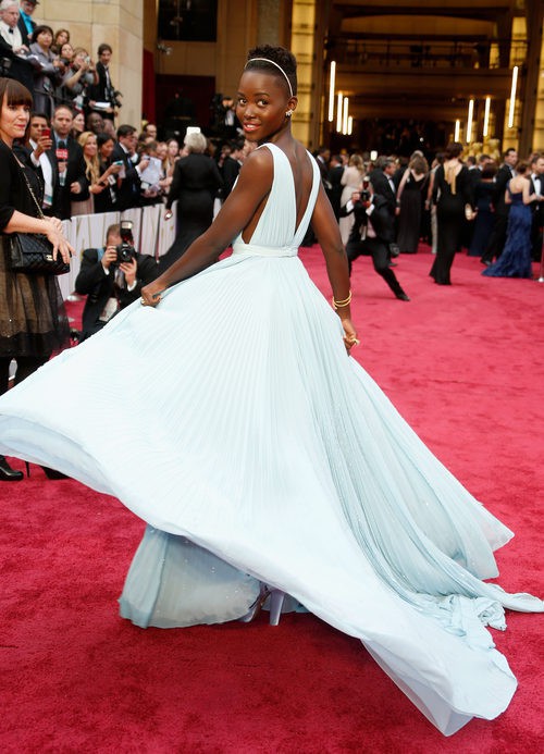 Lupita Nyong'o con vestido de corte griego sin tirantes y plisado con mucho vuelo en color serenity