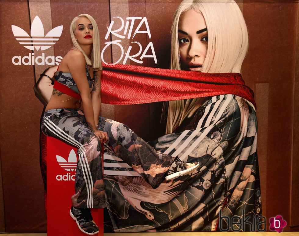 Rita Ora con ropa deportiva posando con el cartel de la nueva campaña para Adidas
