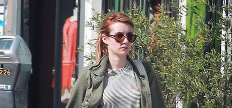 Emma Roberts con abrigo verde militar, pantalón roto y camisa a rayas