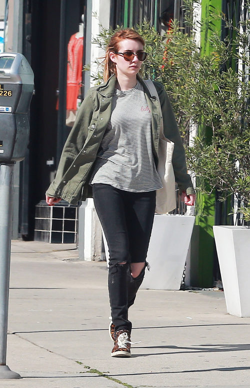 Emma Roberts con abrigo verde militar, pantalón roto y camisa a rayas